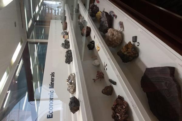 Museum case titled 'Economic Minerals' filled with medium to large mineral specimens distributed across three rows of shelves.