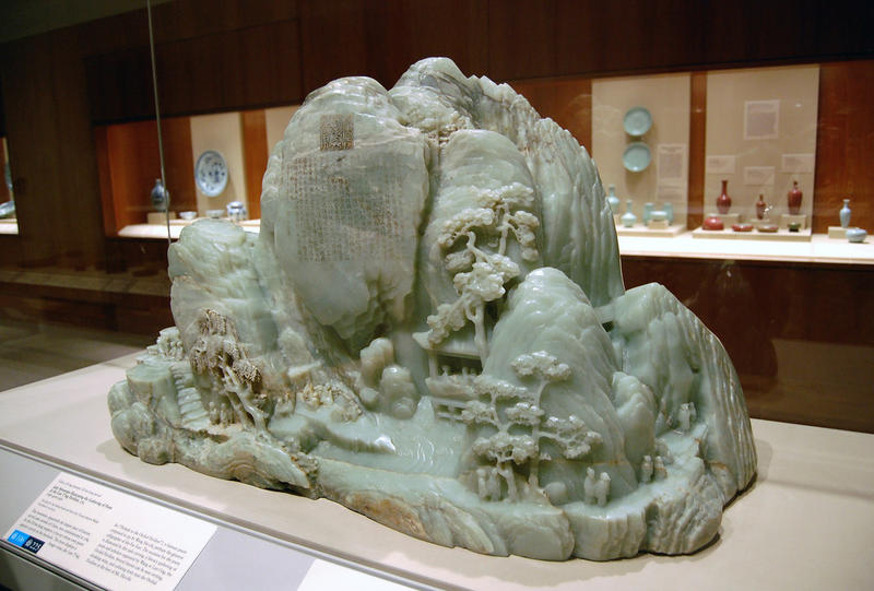 A mountain-side scene, including people and trees, carved out of a pale stone.