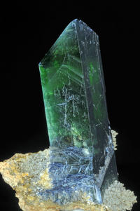 a specimen of prismatic vivianite; it is largely emerald green but transitions to a pale grey-blue at the base